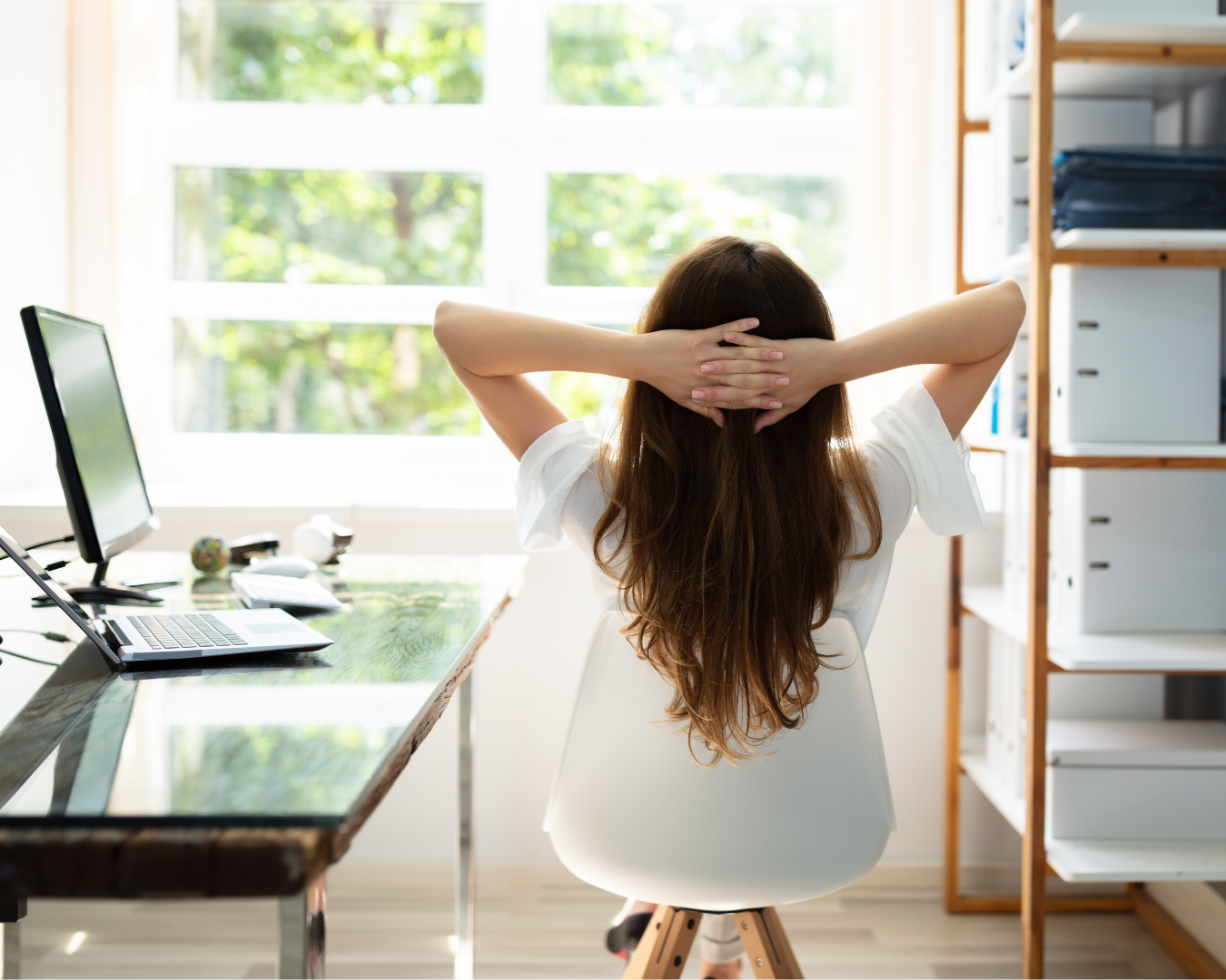 Achtsamkeit im Büroalltag Eine Frau sitzt in ihrem Büro, links der Schreibtisch mit PC, rechts ein Regal, sie in der Mitte mit dem Rücken zur Kamera